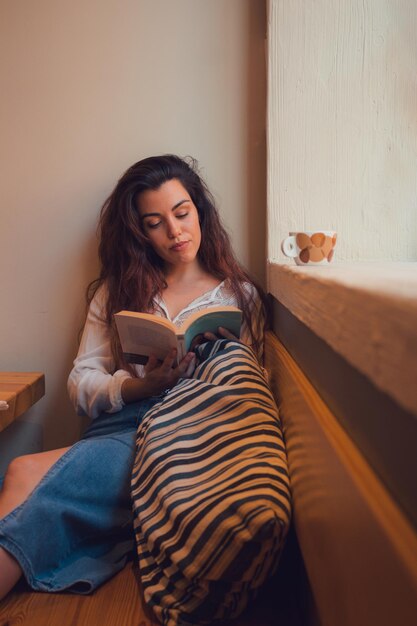 Foto mulher relaxada em uma cafeteria lendo um livro perto de uma janela