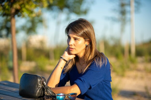 Foto mulher relaxada olhando para longe contemplativa enquanto está sentada ao ar livre em uma mesa na natureza