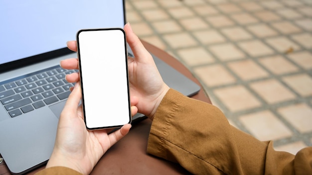 Mulher relaxada sentada do lado de fora usando uma maquete de tela em branco de telefone smartphone