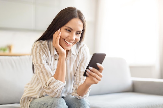 Mulher relaxada sorrindo com smartphone em casa