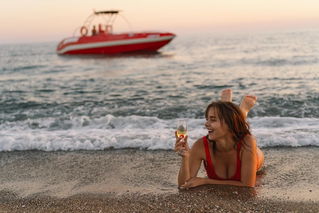 Mulher relaxando com um copo de champanhe na praia durante o pôr do sol