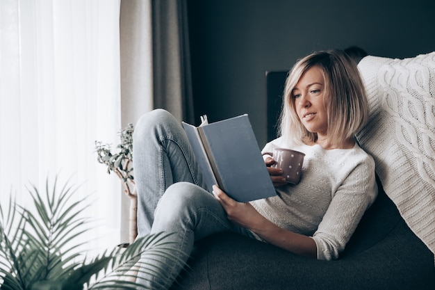 Mulher relaxando lendo um livro e bebendo chá em casa