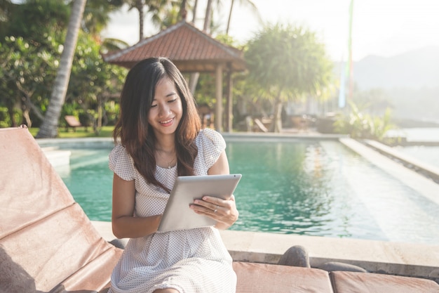 Mulher relaxante ao lado da piscina e usando tablet