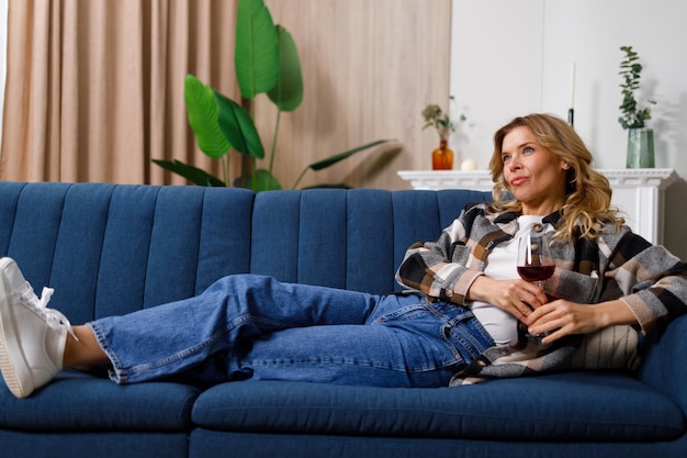 Mulher relaxante com copo de vinho tinto assistindo televisão