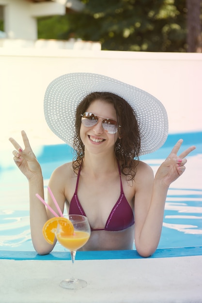 Mulher relaxante e beber um cocktail na piscina