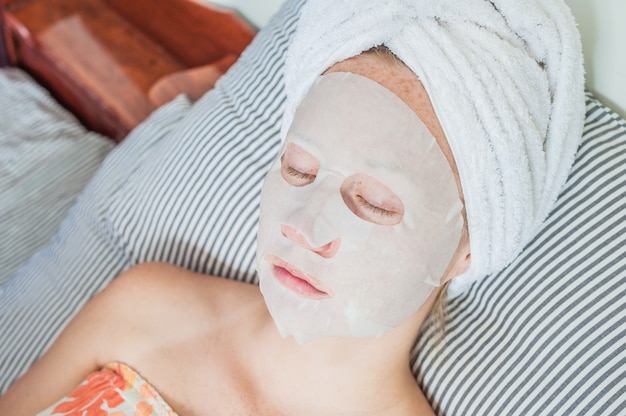 Mulher relaxante na cama com uma máscara facial