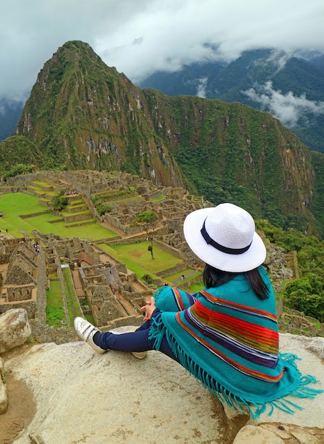 Mulher relaxante no penhasco, olhando para as ruínas incas de machu picchu, cusco, peru