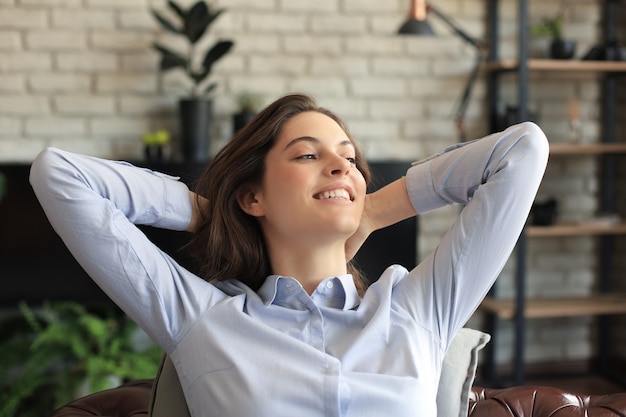 Mulher relaxante sentada confortável no sofá sorrindo. Descansando linda jovem caucasiana.