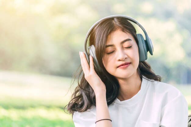 Mulher relaxar com fones de ouvido, ouvindo música, sentado na grama no parque