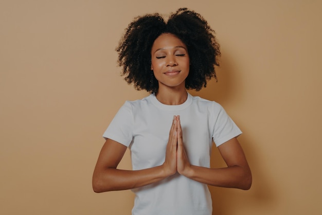 Mulher religiosa afro-americana rezando com as mãos entrelaçadas olhos fechados buscando ajuda