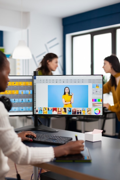 Mulher retocadora negra analisando imagens no pc com dois monitores e retocando ativos digitais com caneta stylus