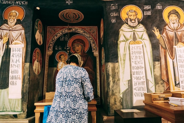 Mulher reza na frente dos ícones no mosteiro de Ostrog, montenegro