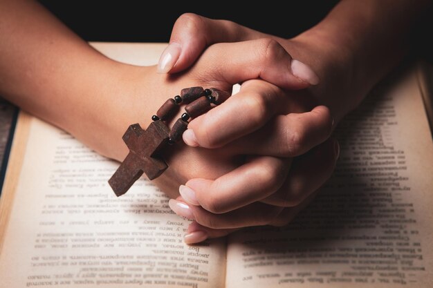 Mulher rezando no livro segurando uma cruz