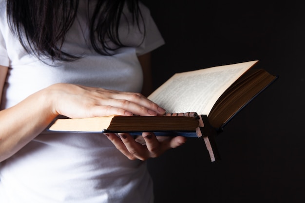 Mulher rezando segurando um livro e uma cruz