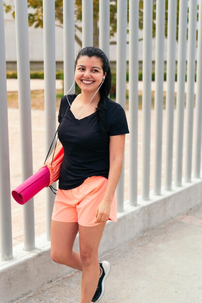 Mulher rindo andando pela rua carregando um tapete de ioga