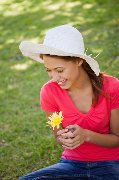 Mulher rindo ao usar um chapéu branco e segurando uma flor amarela