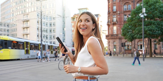 Mulher rindo atraente segurando smartphone andando no meio urbano olhando para o lado Banner recortado vista