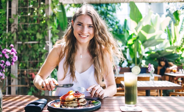 Mulher rindo descansando no café desfrutando de panquecas com molho de frutas e bebendo smoothie refrescante