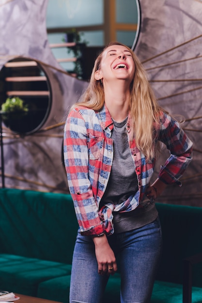 Mulher rindo na camisa Marinha com cabelos cacheados sobre parede branca. Sorriso aberto e lábios vermelhos.