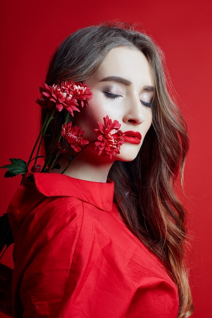 Mulher romântica, com longos cabelos loiros e flores nas mãos em um vestido vermelho, pele limpa e macia