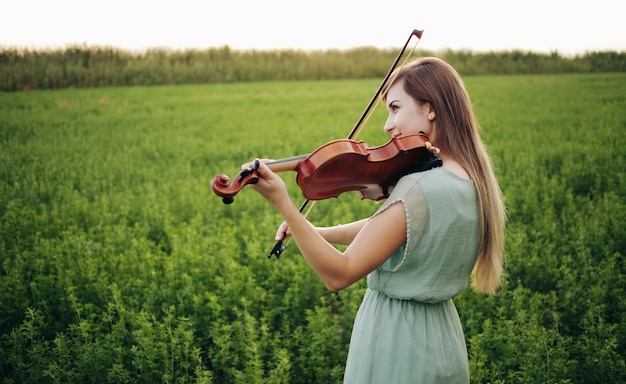 Mulher romântica com o cabelo solto tocando violino. Luz do sol na natureza. Treino de violino