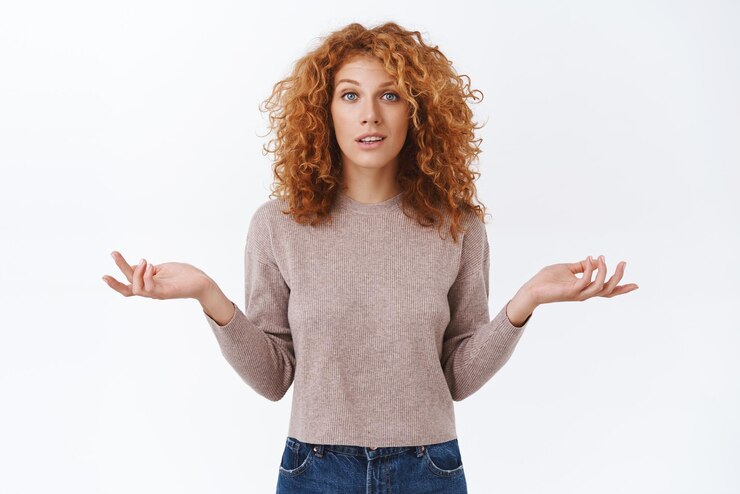 Foto mulher ruiva arrogante indiferente descuidada com cabelo encaracolado usa blusa encolhendo os braços indecisos espalhados de lado parece confuso e incerto tem dúvidas não sei não posso ajudar fundo branco
