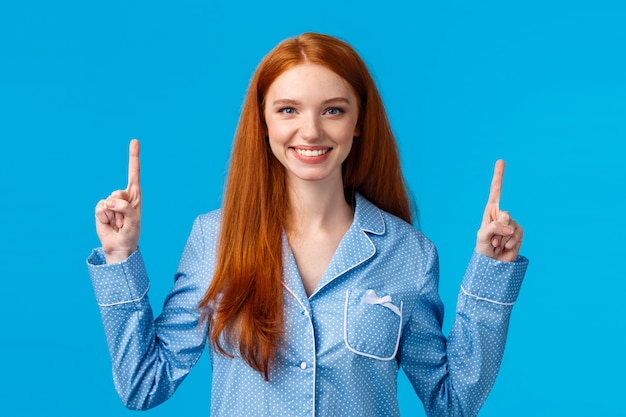 Mulher ruiva bonita carismática e energizada em pijama bonito, apontando os dedos levantados