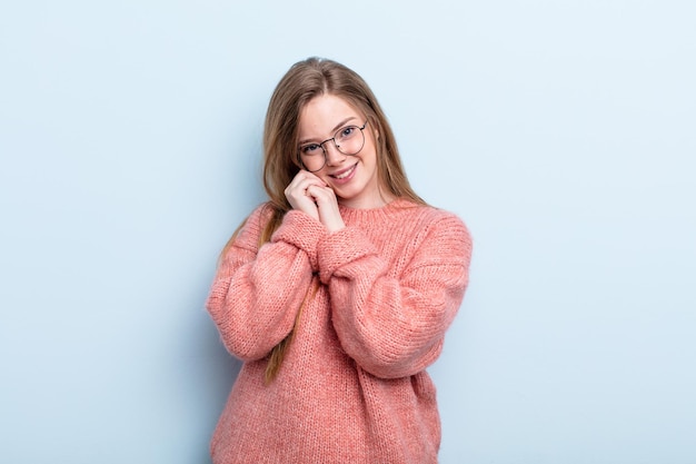 Mulher ruiva caucasiana se sentindo apaixonada e bonita, adorável e feliz, sorrindo romanticamente com as mãos ao lado do rosto