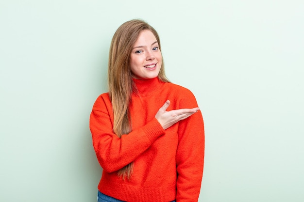 Mulher ruiva caucasiana sorrindo alegremente, sentindo-se feliz e mostrando um conceito no espaço da cópia com a palma da mão