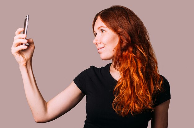 Foto mulher ruiva com uma camiseta preta tirando uma selfie no smartphone