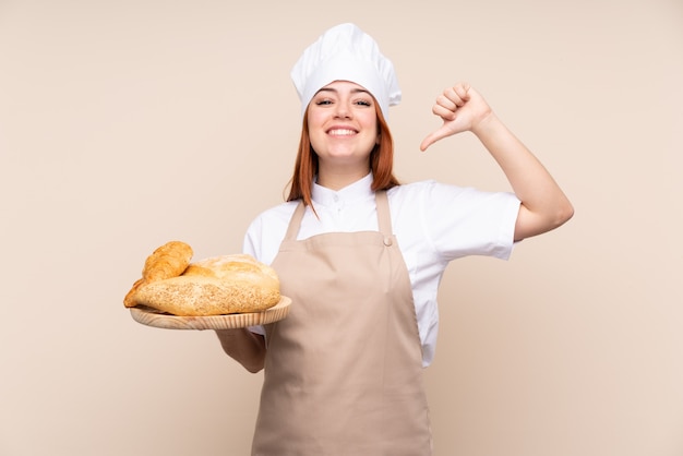 Mulher ruiva de adolescente em uniforme de chef. Padeiro feminino segurando uma mesa com vários pães, orgulhosos e satisfeitos