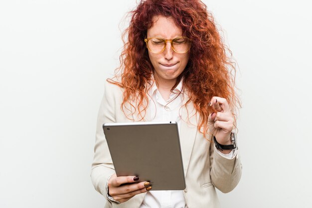 Foto mulher ruiva de negócios caucasiano jovem segurando um tablet cruzando os dedos por ter sorte