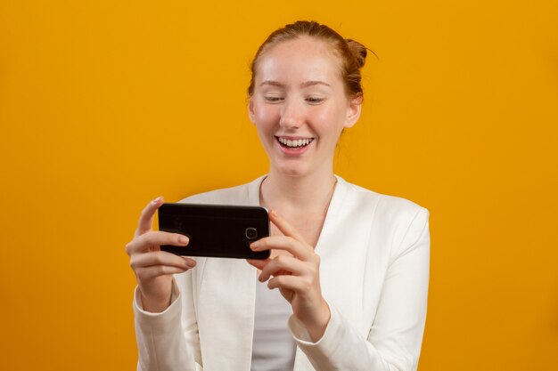 Mulher ruiva de negócios jovem, confiante, bem sucedido e bonito com o smartphone em amarelo. Ocupação, carreira, conceito de trabalho.