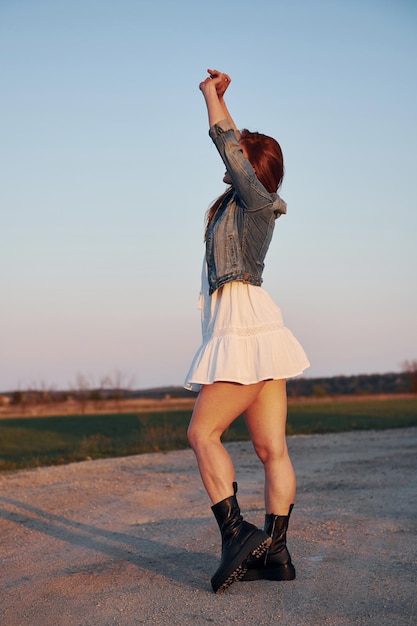 Mulher ruiva de saia em pé e posando para uma câmera na estrada à noite