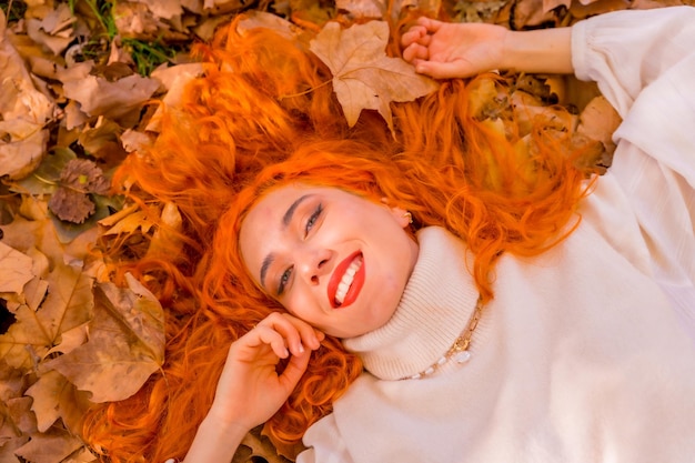Mulher ruiva deitada em folhas no parque da cidade sorrindo estilo de vida da temporada de outono