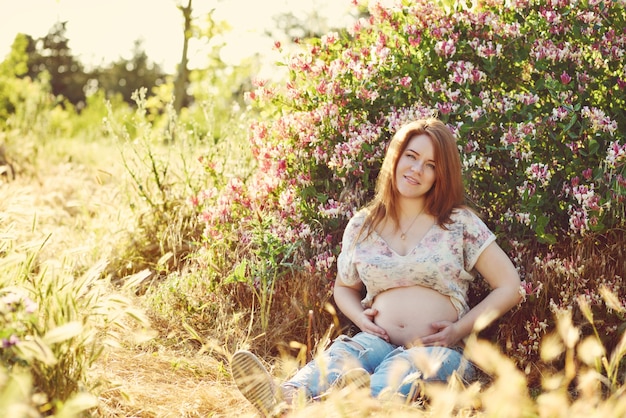 Foto mulher ruiva grávida sentada num prado ensolarado