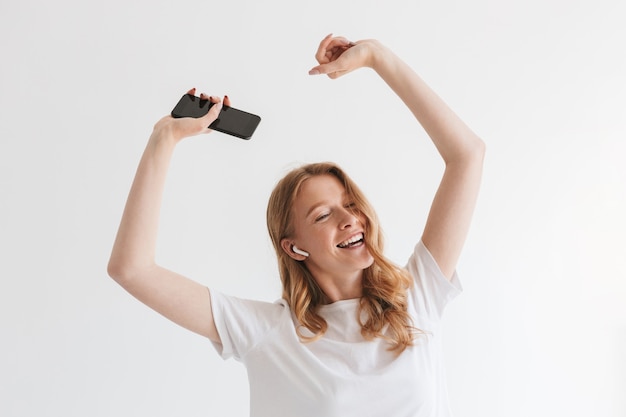 Mulher ruiva jovem feliz ouvindo música com fones de ouvido pelo telefone celular.