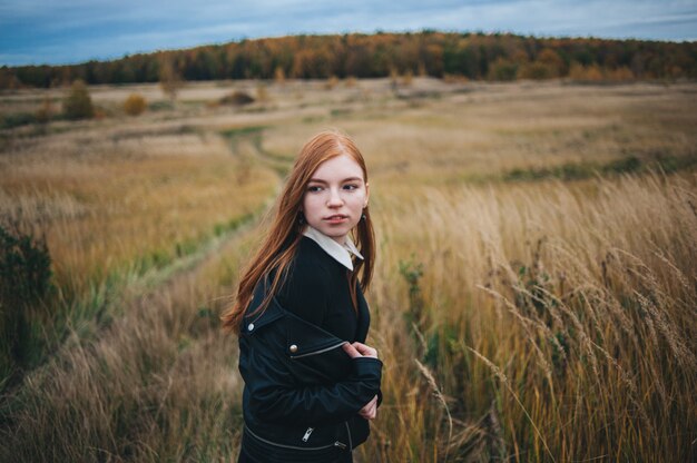 Mulher ruiva linda em um vestido preto caminha em um campo de outono.