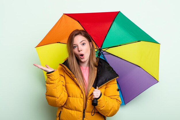 Mulher ruiva parecendo surpresa e chocada, com o queixo caído segurando um objeto. conceito de guarda-chuva