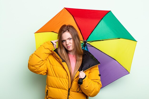 Mulher ruiva se sentindo confusa e confusa, mostrando que você é um conceito de guarda-chuva insano