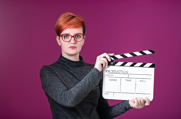 Mulher ruiva segurando badalo de filme isolado contra o conceito de cinema de fundo rosa em estúdio