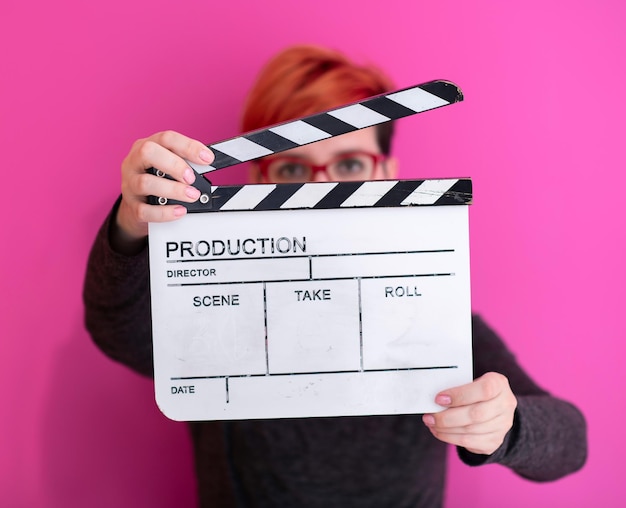 mulher ruiva segurando badalo de filme isolado contra o conceito de cinema de fundo rosa em estúdio