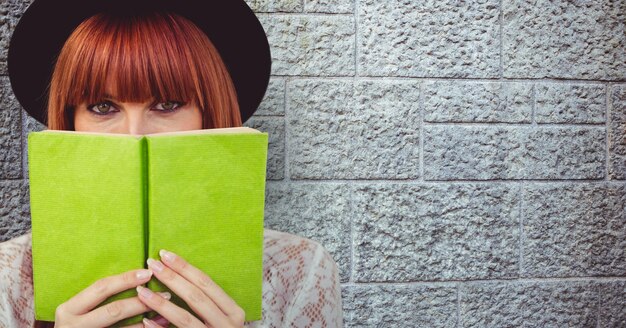 Foto mulher ruiva segurando o livro na frente do rosto contra a parede