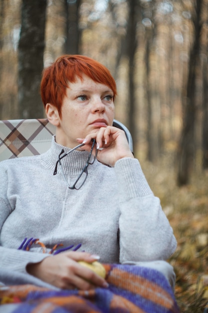 Mulher ruiva sentada em uma espreguiçadeira dobrável em um fundo de floresta outono