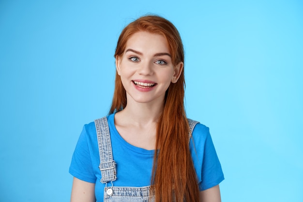 Mulher ruiva simpática, confiante e agradável, olhando para a câmera, sorrindo alegremente, conversar com o cliente, dar conselhos, ficar otimista, bom humor positivo, fundo azul, sorriso divertido