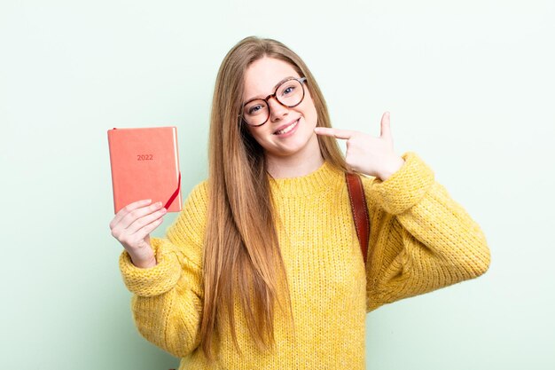 Mulher ruiva sorrindo com confiança apontando para o próprio conceito de planejador de sorriso amplo