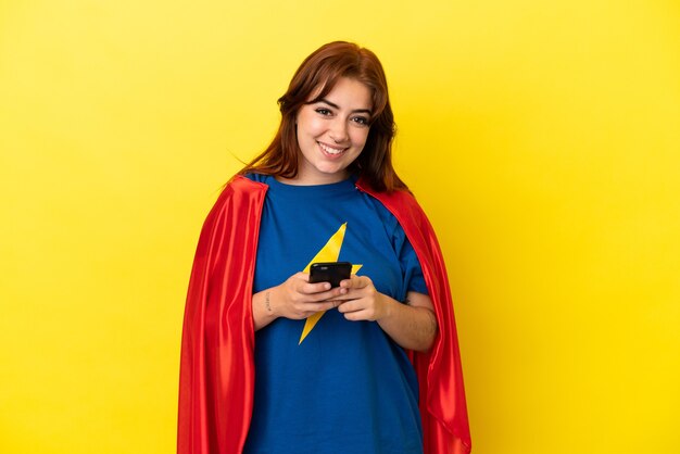 Mulher ruiva super-heroína isolada em fundo amarelo enviando uma mensagem com o celular