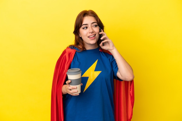 Mulher ruiva super-heroína isolada em um fundo amarelo segurando um café para levar e um celular