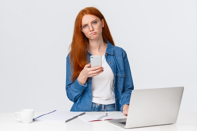 Mulher ruiva tem dúvidas sobre a idéia segurando o smartphone