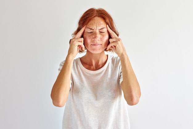 Mulher ruiva tenta se lembrar, ficar pensando, segurando os dedos na têmpora, isolado no branco